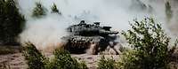 Battle tank Leopard A2 In the terrain between bushes, a camouflaged battle tank Leopard A2 drives, the combat turret is swung to the left.