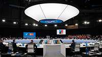 Participants of a NATO meeting are sitting in a conference room around a large round table.
