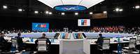 Participants of a NATO meeting are sitting in a conference room around a large round table.