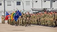Mehrere Soldaten stehen in Formation zum Antreten eines Appells. Vor Ihnen Soldaten die maschieren.