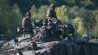 in Schutzausrüstung gekleidete Soldaten sitzen auf einem Schützenpanzer Marder, im Hintergrund ist Laubwald zu erkennen.