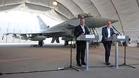 Boris Pistorius und Andris Sprūds geben ein Statement, hinter ihnen steht ein Kampfflugzeug vom Typ Eurpfighter.