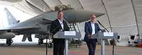 Boris Pistorius und Andris Sprūds geben ein Statement, hinter ihnen steht ein Kampfflugzeug vom Typ Eurpfighter.