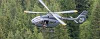 Über einen Tannenwald fliegt ein Leichter Kampfhubschrauber H145M. Die Aufnahme wurde aus der Luft gemacht.