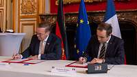 Boris Pistorius und Sébastian Lecornu sitzen an einem Tisch und unterzeichnen ein Dokument.