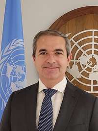 Eine männliche Person lächelt für eine Portraitaufnahme in die Kamera.