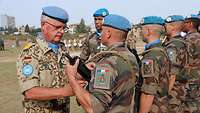 Ein deutscher UN-Soldat steckt einem französischen UN-Soldaten eine Medaille an.