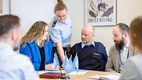 Sechs Personen, darunter zwei Soldaten besprechen sich an einem Tisch. 