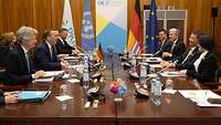 Boris Pistorius und Phumtham Wechayachai sitzen sich mit ihren Delegationen an einem Tisch gegenüber und unterhalten sich.