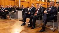 Johann Wadepuhl, António Guterres und Boris Pistorius sitzen in der ersten Reihe eines Publikums und schauen zur Bühne.