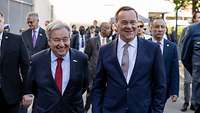 Pistorius und Guterres laufen lächelnd nebeneinander.