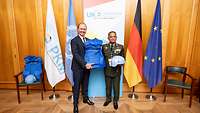 Staatssekretär Hilmer überreicht Weste und Helm an einen asiatischen Soldaten 