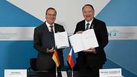 Boris Pistorius und Gilberto C. Teodoro stehen nebeneinander und halten unterzeichnete Dokumente zum Betrachter.