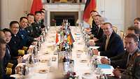Admiral Dong Jun und Boris Pistorius sitzen sich mit ihren Delegationen am Tisch gegenüber.
