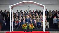 German Chancellor, Friedrich Merz speaks at a lectern, soldiers and politicians are sitting behind him.