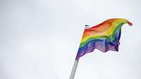 vor grauem Himmel weht eine Regenbogenflagge.