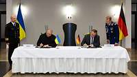 Rustem Umerov und Boris Pistorius sitzen an einem Tisch und unterzeichnen Dokumente.