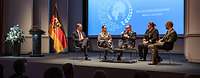 fünf Personen auf einer kleinen Konzertbühne während einer Podiumsdiskussion neben Rednerpult und Deutschlandflagge