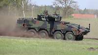 Ein Radpanzer fährt im Gelände und wirbelt Staub auf