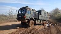 Ein Transportfahrzeug der Bundeswehr, fährt schräg zum Betrachter auf offenem Gelände.
