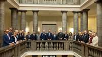Vertreter der Bundesregierung und weitere Personen stehen in der Säulenhalle für ein Gruppenfoto.
