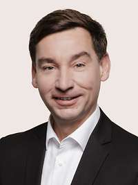 Sebastian Hartmann schaut für eine Portraitaufnahme freundlich in die Kamera.