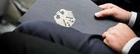 Close-up of a person in a suit, holding a briefcase with an emblem.