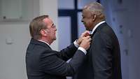 Boris Pistorius bringt den Verdienstorden an Lloyd Austins Anzugsjacke an.