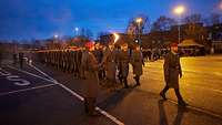 Mehrere Soldaten marschieren in Dunkelheit auf einem Paradeplatz im Rahmen eines Feierlichen Gelöbnis