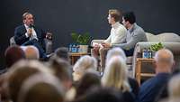 Boris Pistorius und zwei Personen unterhalten sich auf einer Bühne, im Vordergrund sitzt Publikum.
