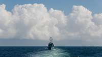 Auf offenem Gewässer ist ein Minentauchereinsatzboot am Horizont frontal zum Betrachter zu erkennen.