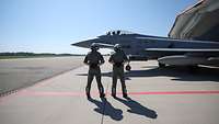 Zwei Soldaten stehen vor einem seitlich stehenden Eurofighter auf einem Flugplatz.
