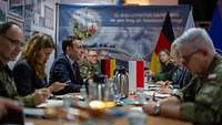 Mehrere Personen und Soldaten sitzen an einem langen Tisch. Die Flaggen von Deutschland und Polen stehen auf dem Tisch.