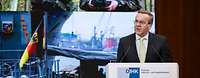 Boris Pistorius steht am Rednerpult und spricht. Im Hintergrund sind Fotos mit Soldaten zu sehen.