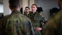 Ein General steht einem Soldaten gegenüber und spricht mit ihm, weitere Soldaten hören zu.