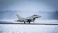 Ein Kampfflugzeug vom Typ Eurofighter startet auf der Startbahn in einer winterlichen Landschaft.