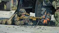 Ein Soldat liegt am Boden neben einem Fahrzeug und feuert mit dem Maschinengewehr.