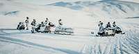 Gruppe vom Soldaten im Schneetarnanzug steht mit Schneemobilen in einer verschneiten Landschaft.
