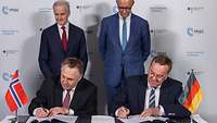 Boris Pistorius und Tore O. Sandvik sitzen nebeneinander und unterzeichnen jeder ein Dokument.