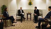 Boris Pistorius und Chan Chun Sing sitzen mit anderen Personen in einem Raum und unterhalten sich.