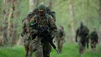 Ein Soldat in vollständiger Ausrüstung und mit verdecktem Gesicht läuft durch einen Wald