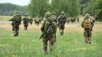 Soldaten laufen mit voller Ausrüstung und Waffen über eine Wiese