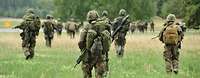 Soldaten laufen mit voller Ausrüstung und Waffen über eine Wiese
