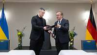Minister Pistorius und sein ukrainischer Amtskollege tauschen schwarze Dokumentenmappe aus.