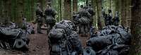 Rucksäcke von Soldaten liegen und stehen auf dem Waldboden. Im Hintergrund sind Soldaten zu sehen.