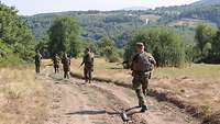 Soldaten des Einsatzkontingents laufen Patrouille auf einem sandigen Weg. Im Hintergrund sind Berge.
