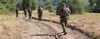 Soldaten des Einsatzkontingents laufen Patrouille auf einem sandigen Weg. Im Hintergrund sind Berge.