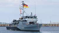 Ein Boot der Marine mit Soldaten an Deck fährt in einem Gewässer an einer Kaimauer vorbei.