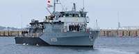 Ein Boot der Marine mit Soldaten an Deck fährt in einem Gewässer an einer Kaimauer vorbei.