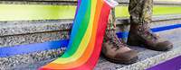 Eine Regenbogenfahne liegt auf einer Treppe, dahinter sind die Beine einer Soldatin zu sehen.